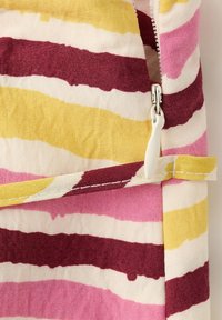 Gros plan sur un tissu à rayures jaunes, bordeaux, roses et blanches avec une fermeture éclair blanche et un détail de boucle en tissu assorti.