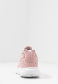 Zapatilla deportiva rosa con parte superior de malla transpirable, talón acolchado y suela de goma blanca. Detalles texturizados en los laterales.