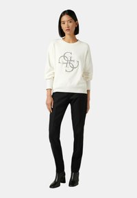 Suéter blanco con un diseño gráfico en un tono metálico, combinado con pantalones negros de corte recto y botines negros. Textura de tejido suave.