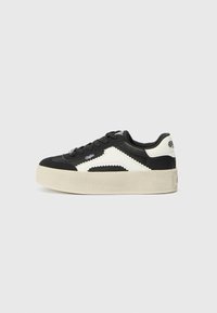 Svart og hvit sneakers med glatt lærøvre, zigzag-mønstrede detaljer, rund tå, og en tykk kremfarget gummi såle.
