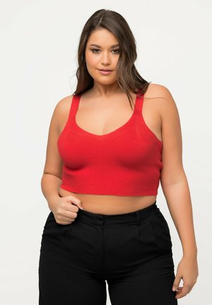 Rode cropped tanktop met brede banden, geribbelde textuur en een V-hals ontwerp. Gepaard met zwarte hooggetailleerde broek. Eenvoudig en modern.