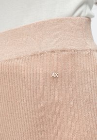 Svetloružová rebrovaná pletená látka s hrubým pásom a malým bielym logom "AX" na boku. Jemná textúra s viditeľnými jemnými líniami.