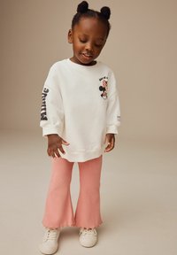 Vit sweatshirt med en Mickey Mouse-grafik, kombinerad med rosa ribbade utsvängda byxor. Stylad med vita sneakers. En enkel, avslappnad outfit.