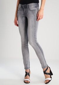 Jeans de mezclilla gris en corte slim con un sutil patrón desgastado y diseño clásico de cinco bolsillos, combinados con sandalias de tacón en negro y blanco.