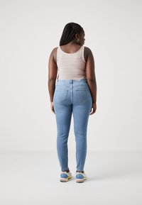 Blue denim jeans with a high waist, fitted silhouette, and two back pockets. Paired with a multicolored striped tank top and athletic shoes.