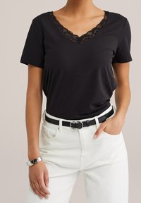 Black short-sleeve t-shirt with a lace-trimmed V-neck, paired with white high-waisted jeans and a black belt featuring a silver circular buckle.