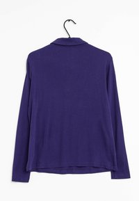 Långärmad lila skjorta i mjuk bomull, med krage och rak nederkant med sidofickor. Hänger från en svart krok.