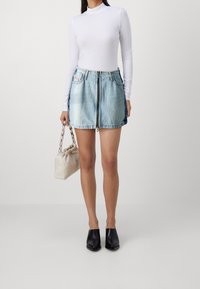 Ljusblå denimkjol med dragkedja fram, två sidofickor och fransad nederkant. Sammansatt med en vit långärmad topp och svarta slip-on skor.