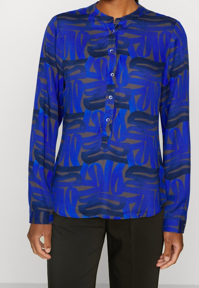 Blue patterned blouse with long sleeves and a mandarin collar, featuring abstract designs in varying shades of blue and dark accents.