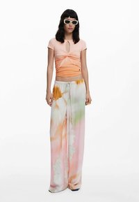 Fersken- og orangefarvet knyttet cropped top kombineret med løse, flerfarvede tie-dye bukser med pink, grønne og gule nuancer.