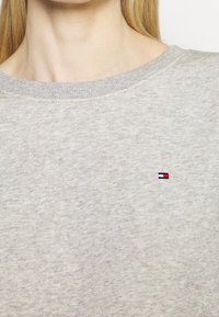 Grijze katoenen sweater met een geribbelde ronde hals. Bevat een klein, kleurrijk logo op de borst. Zachte textuur en een relaxte pasvorm.