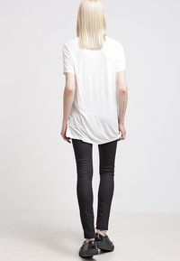 Vit t-shirt med kort ärm och rundad nederkant, kombinerad med svarta skinny jeans och svarta skor, sedd bakifrån.