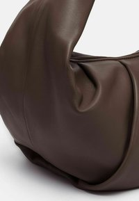 Borsa a tracolla in pelle marrone con una finitura morbida e testurizzata, caratterizzata da un manico sovradimensionato distintivo e un dettaglio arricciato su un lato.
