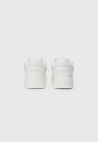 Hvite sneakers med glatt syntetisk materiale, med polstret krage, tonet søm og preget "GUESS"-logo på hælen.