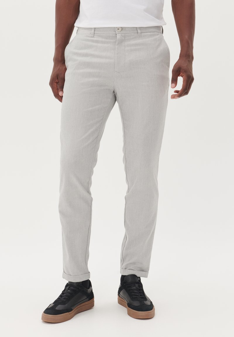 Jasnoszare spodnie na miarę o subtelnej fakturze, z prostą nogawką i zapięciem na guzik, zestawione z czarnymi trampkami z brązowymi podeszwami.