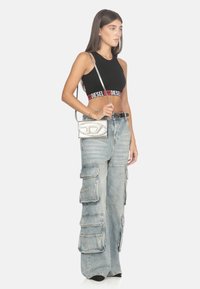 Top corto nero con logo "DIESEL", jeans cargo a vita alta di colore blu chiaro con diverse tasche, e una borsa a tracolla argentata.