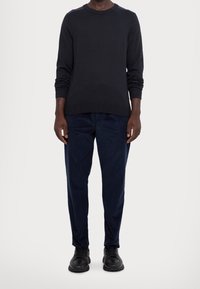 Dark gray knitted sweater with ribbed cuffs and crew neck, paired with navy tapered pants, completing the look with black sneakers.
