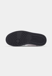 Semelle en caoutchouc noire d'une chaussure Nike avec des motifs de bande de roulement circulaires et en grille, et le logo Nike en relief près du centre.