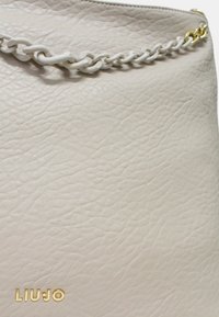 Borsa a tracolla in pelle grigia chiara con superficie texture, dotata di manico a catena bianca e accessori in oro. Logo del marchio in oro sul fondo.