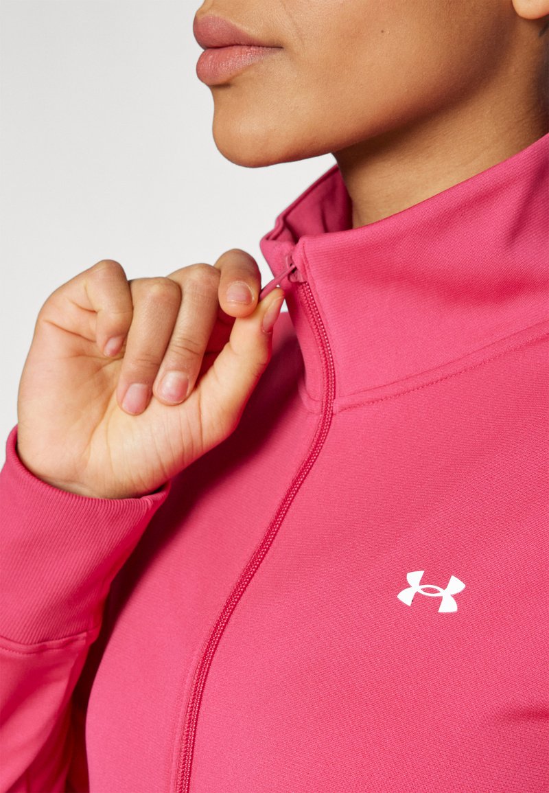 Giacca sportiva rosa aderente con colletto con zip e logo bianco. Texture liscia con polsini a costine e dettagli di cucitura in evidenza.