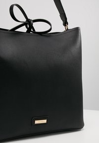 Sac fourre-tout en cuir noir avec de fines bretelles et une petite plaque de marque rectangulaire dorée portant l’inscription « ALDO » dans le coin inférieur avant.