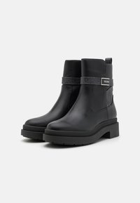 Botas negras de cuero hasta el tobillo con una suela de plataforma gruesa, que cuentan con una correa decorativa y un detalle del logo en el lateral. Textura suave y diseño duradero.