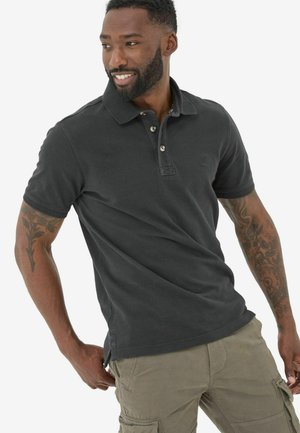 Schwarzes Polohemd mit Dreiknopf-Leiste, kurzen Ärmeln und Logo auf der Brust. Getragen mit olivenfarbigen Cargo-Hosen, die Taschen und eine lässige Passform haben.