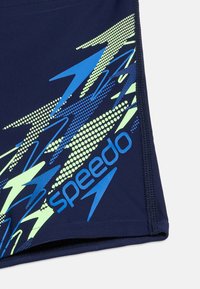 Ναυτικό μπλε ύφασμα με το λογότυπο Speedo και αφηρημένα σχέδια κεραυνών σε μπλε και πράσινο σε μαγιό.