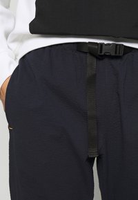 Námořnické šortky vyrobené z texturované látky mají nastavitelný černý pásek. Design zahrnuje malý žlutý akcent poblíž kapsy.