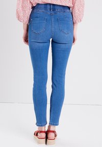 Schmale blaue Jeans mit hoher Taille, die eine glatte Denim-Textur, zwei Gesäßtaschen und eine leichte Verjüngung am Knöchel aufweisen.