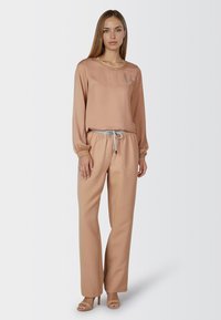 Beige long-sleeve blouse with a simple round neckline and subtle embroidery; paired with matching beige wide-leg pants featuring a drawstring waist.
