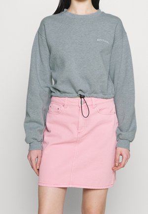Vrouw die een grijze cropped sweatshirt met lange mouwen en trekkoord draagt, gecombineerd met een roze denim minirok met hoge taille.