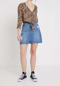 Brown and black patterned blouse with a V-neck and tie front, paired with a denim skirt featuring distressed accents and a flared shape.