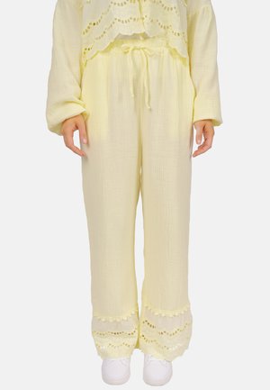 Gelbe, leichte, strukturierte Hose mit einem Kordelzug am Bund und Spitzenbesatz am Saum, kombiniert mit weißen Turnschuhen.