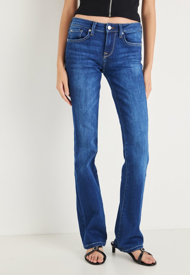 Niebieskie dżinsy typu flare z średnim stanem, pięcioma kieszeniami i kontrastowymi szwami. Gładka faktura z delikatnym przetarciem na udach.