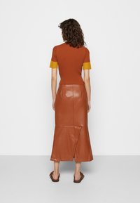 Ruskea raidoitettu lyhythihainen paita, jossa on keltaisia kudottuja yksityiskohtia, yhdistettynä ruskeaan nahkais maxi-hameeseen, jossa on sivuhaalari ja sileä pinta.