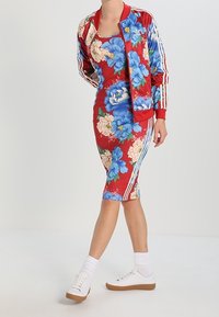 Röd blomstrig bomberjacka med blå och krämfärgade blommor; figurnära klänning med samma mönster. Matchas med vita sneakers och randiga träningsstrumpor.