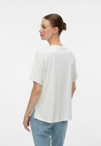 T-shirt bianco a maniche corte in tessuto morbido, con scollatura rotonda e orlo posteriore leggermente più lungo. Abbinato a jeans azzurri.