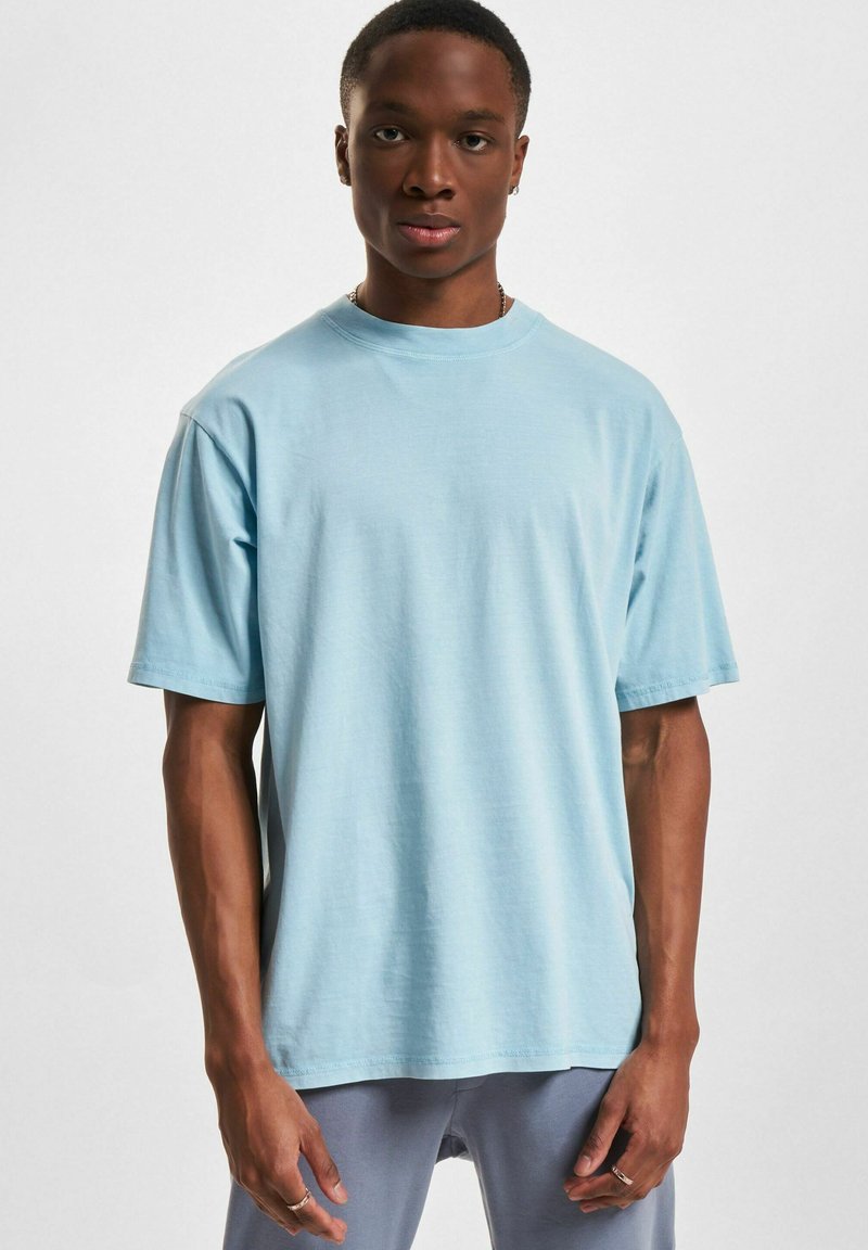 Lichtblauwe katoenen t-shirt met korte mouwen, een relaxte pasvorm, ronde hals en een gladde textuur. Gecombineerd gedragen door een model.