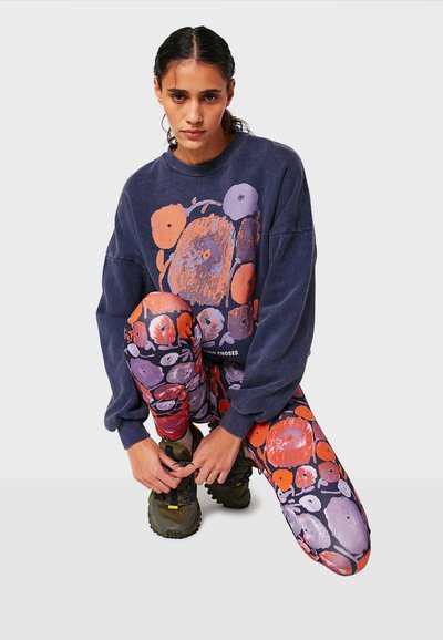 Felpa oversize navy con stampa floreale abbinata a leggings multicolori con motivi astratti, completata da sneakers verdi.