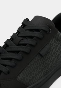 Tenis cu sireturi plate, un superior texturat și panouri laterale cu model de logo. Are o talpă netedă și materiale durabile.