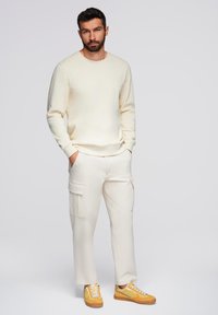 Creme sweatshirt, creme cargo bukser med lommer og gule sneakers med hvide snørebånd. Enkel design, blød tekstur og afslappet pasform.