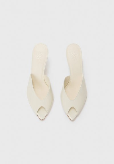 Mule cu vârf deschis, din piele moale, de culoare albă-întunecată. Prezintă decupaje unghiulare și un design minimalist, neted. Solea este ușor căptușită pentru confort.