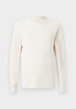 Long-sleeve, ribbed top in off-white with a crew neckline. Features subtle "GAP" logo on the chest. Soft texture and fitted design.