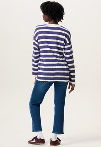 Chemise à manches longues rayée en violet et blanc, avec une coupe décontractée. Associée à un jean bleu et des chaussures foncées. Texture de tissu lisse.