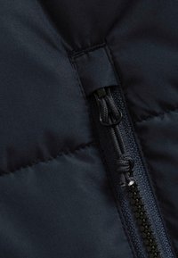 Tissu rembourré bleu marine avec une fermeture éclair visible. La fermeture éclair est dotée d'une tirette noire et de cordons tressés, mettant en valeur une texture lisse.
