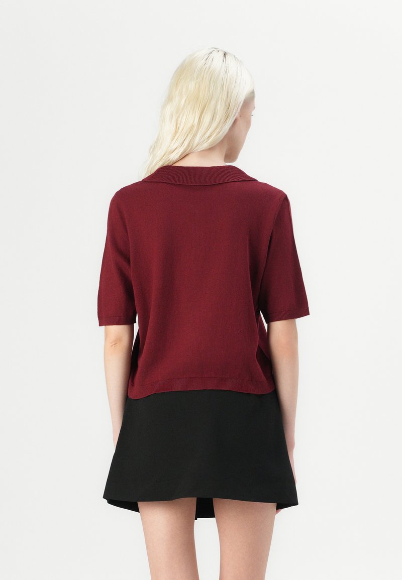 Bordowy sweter z kołnierzykiem i krótkimi rękawami, zestawiony z czarną spódnicą rozkloszowaną. Gładka tekstura, średnia długość i swobodny krój.