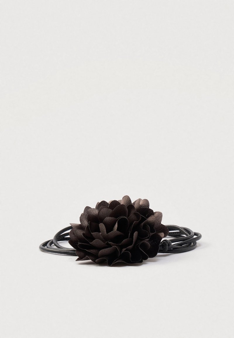 Mustast kiulisest materjalist kihiline lillemotiiviga juukseaksessuaar, kinnitatud mustale elastikpaelale.