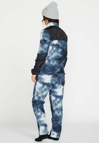 Fleece-Jacke und -Hosen-Set in Marineblau mit einem Batikmuster. Verfügt über ein einfarbiges schwarzes Oberteil und eine weiche Textur. Enthält eine graue Strickmütze.