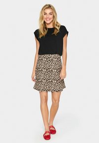 Schwarzes Kurzarmoberteil, kombiniert mit einem beigefarbenen Leopardmuster-Rock; rote Ballerinas. Glattes Material, lässige Passform, kurze Länge und ausgestellte Form.